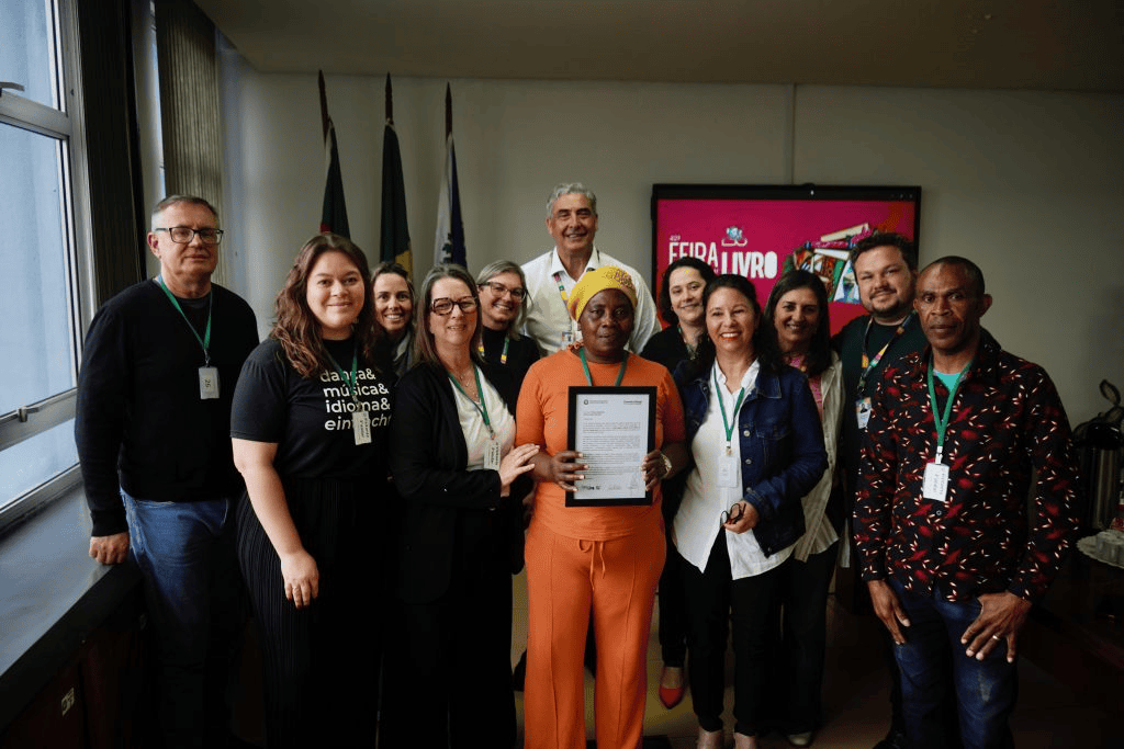 Grupo posa com certificado diante de painel da Feira do Livro de Campo Bom