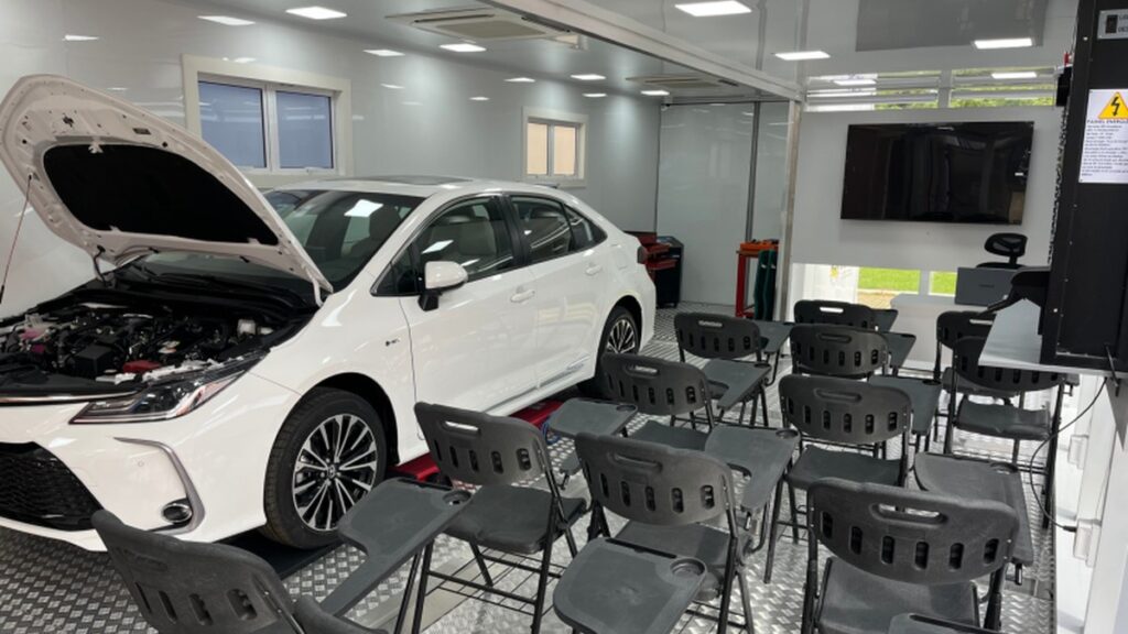 Interior da unidade móvel do Carretas do Saber, com automóvel de capô aberto e equipamentos para aulas sobre veículos eletrificados.