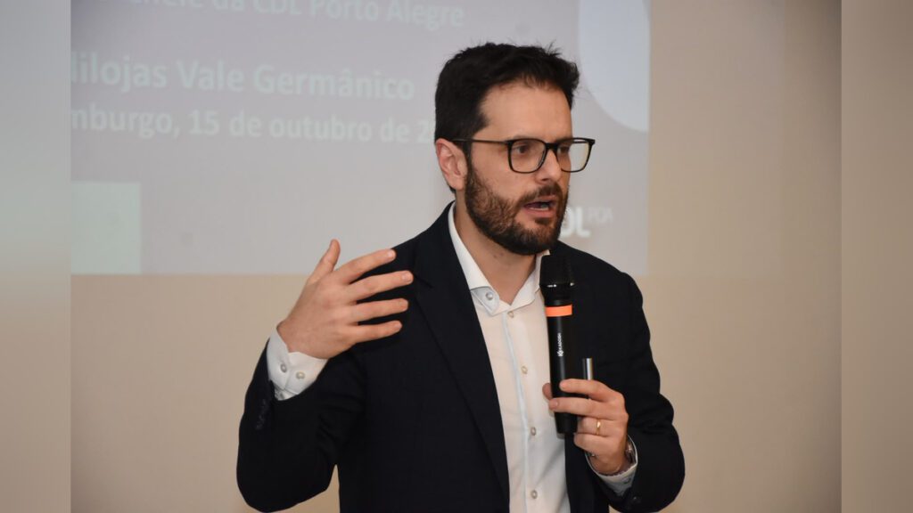 Custo do trabalho é tema de encontro com empresários em Novo Hamburgo Oscar Frank fala ao microfone sobre custo do trabalho em encontro do Sindilojas Vale Germânico.