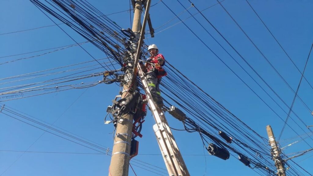 Trabalhador em escada realiza retirada de fios sem uso em poste na Avenida Pedro Adams Filho